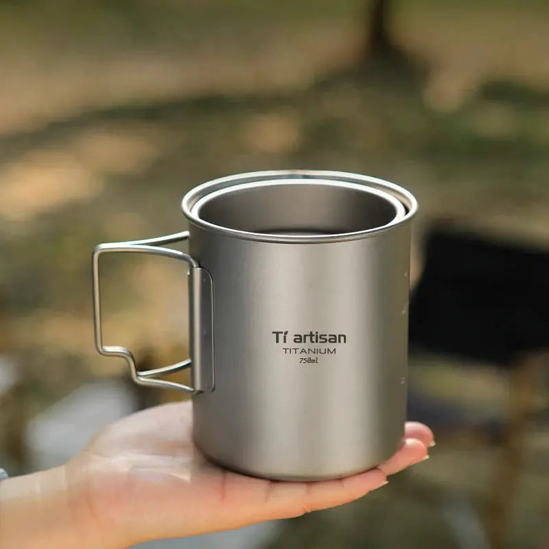 Tiartisan titanium camping mug with folding handle, 750ml, held in hand outdoors.