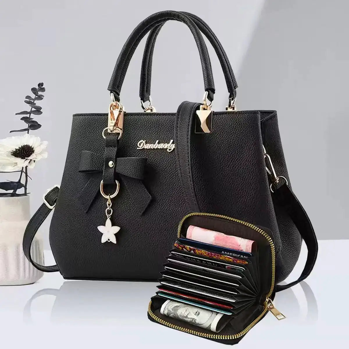 Black pebbled faux-leather handbag with bow charm, gold hardware, Danbody logo, top handles; 2-piece with wallet.
