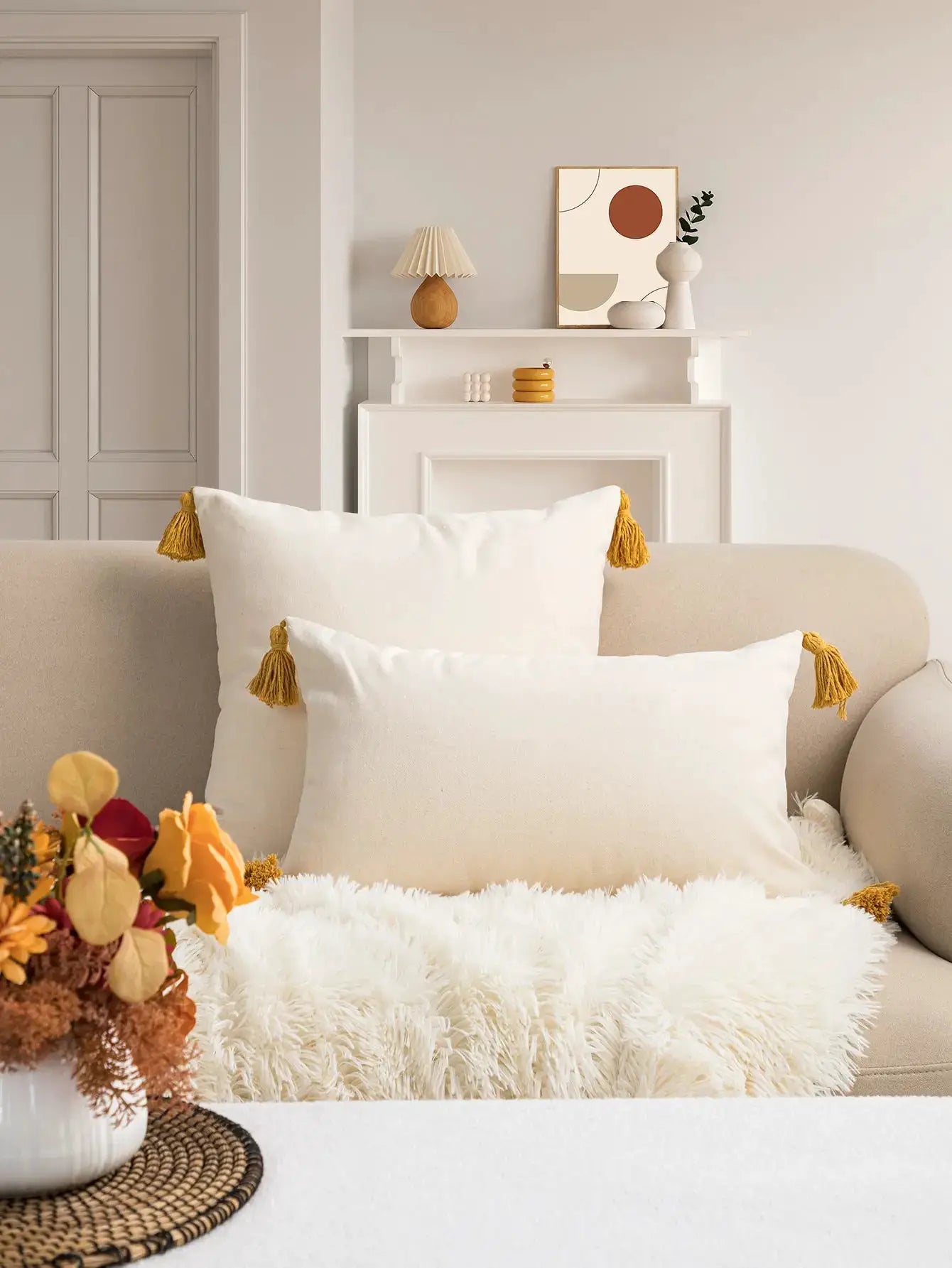 Pillow covers: white fabric with mustard tassels on the corners, placed on a beige sofa in a neutral living room
