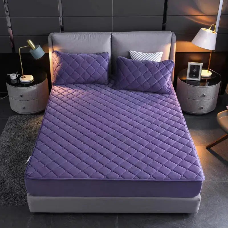 Plush purple velvet quilted mattress cover by Simples Market with two matching pillows on a grey bed.
