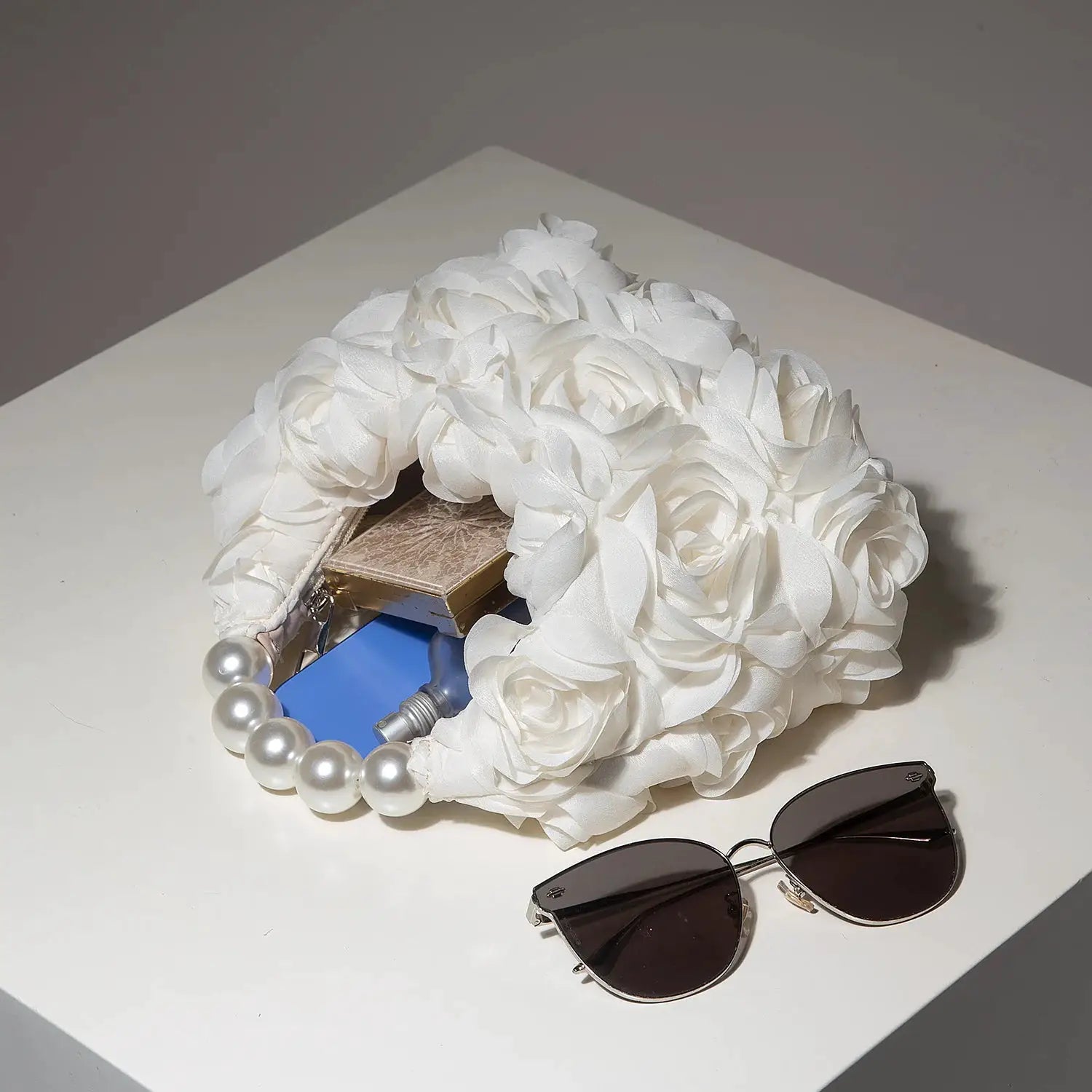 White floral petal clutch bag with pearl handle; sunglasses nearby