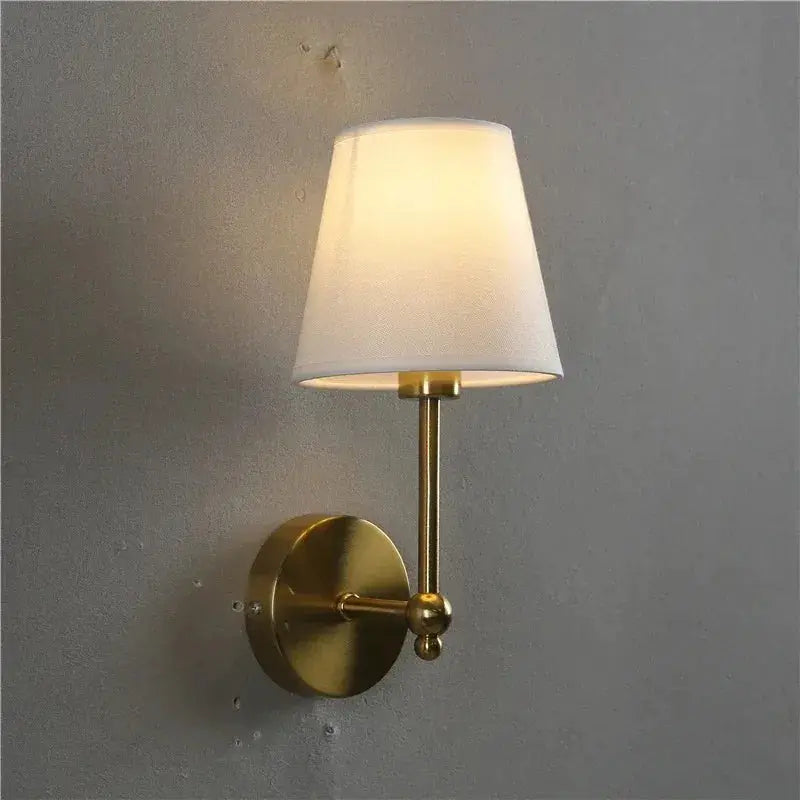 Brass wall lamp sconce with white fabric shade for bedroom or bathroom.