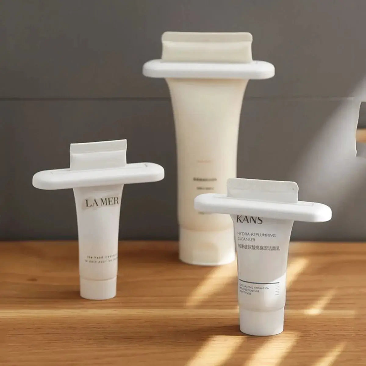 Toothpaste squeezer trio in white plastic, with La Mer and KANS toothpaste tubes visible