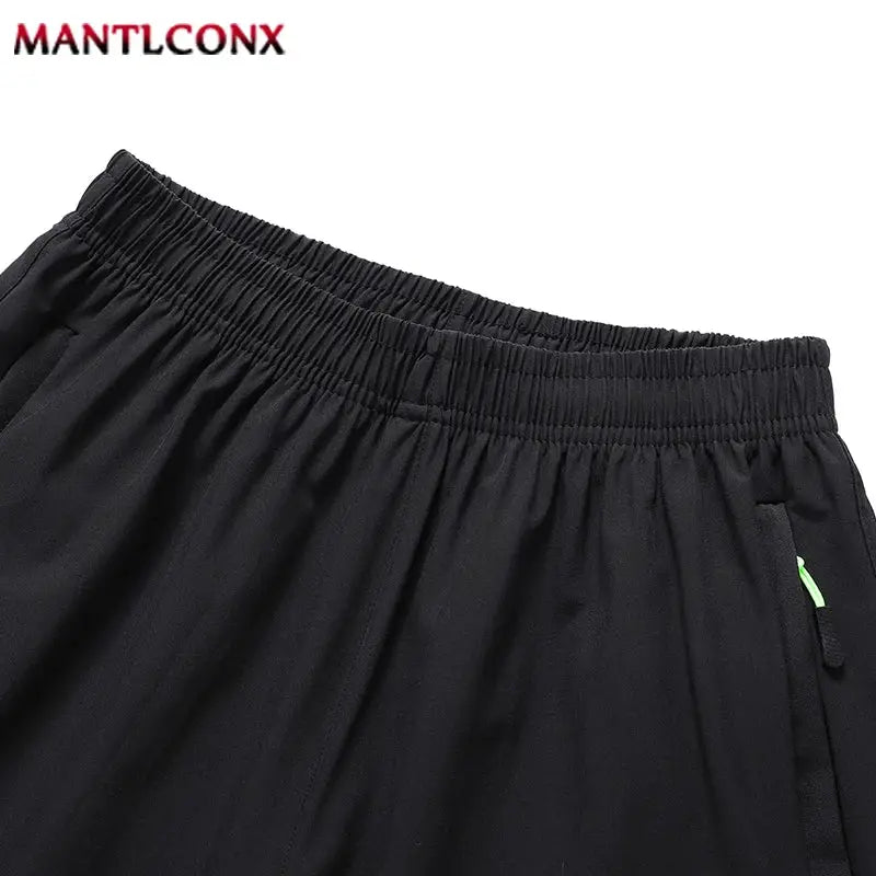 Men's black quick-dry jogging shorts by MANTLCONX; elastic waist, breathable lightweight fabric, neon zipper pull