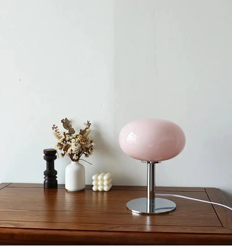 Pink macaron glass table lamp with chrome stem and round base on a wooden desk