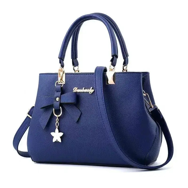 Blue bow-accent handbag by Simples Market with gold logo, top handles and detachable shoulder strap.