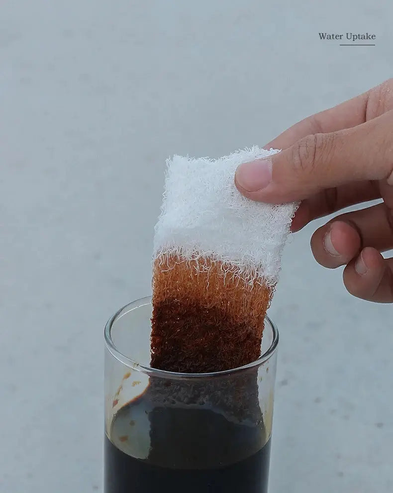 Simples Market first aid compressed sterile gauze roll, white Z-folded, being dipped into a glass of dark liquid.