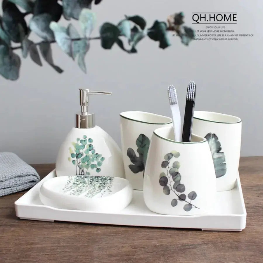 White ceramic bathroom set with green botanicals by QH.HOME; soap dispenser, three holders, mouthwash cup and tray