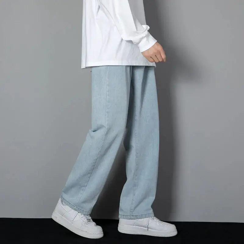 Men's light blue wide-leg denim jeans, side profile with white sneakers and white shirt.