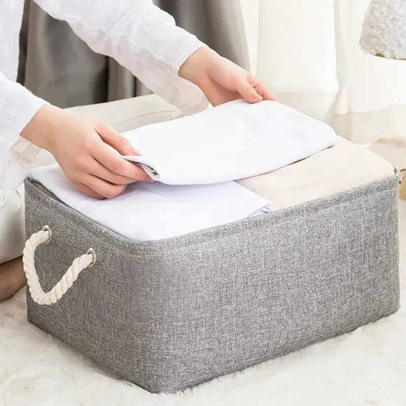Folding linen fabric storage basket with rope handles in gray, holding folded white linens