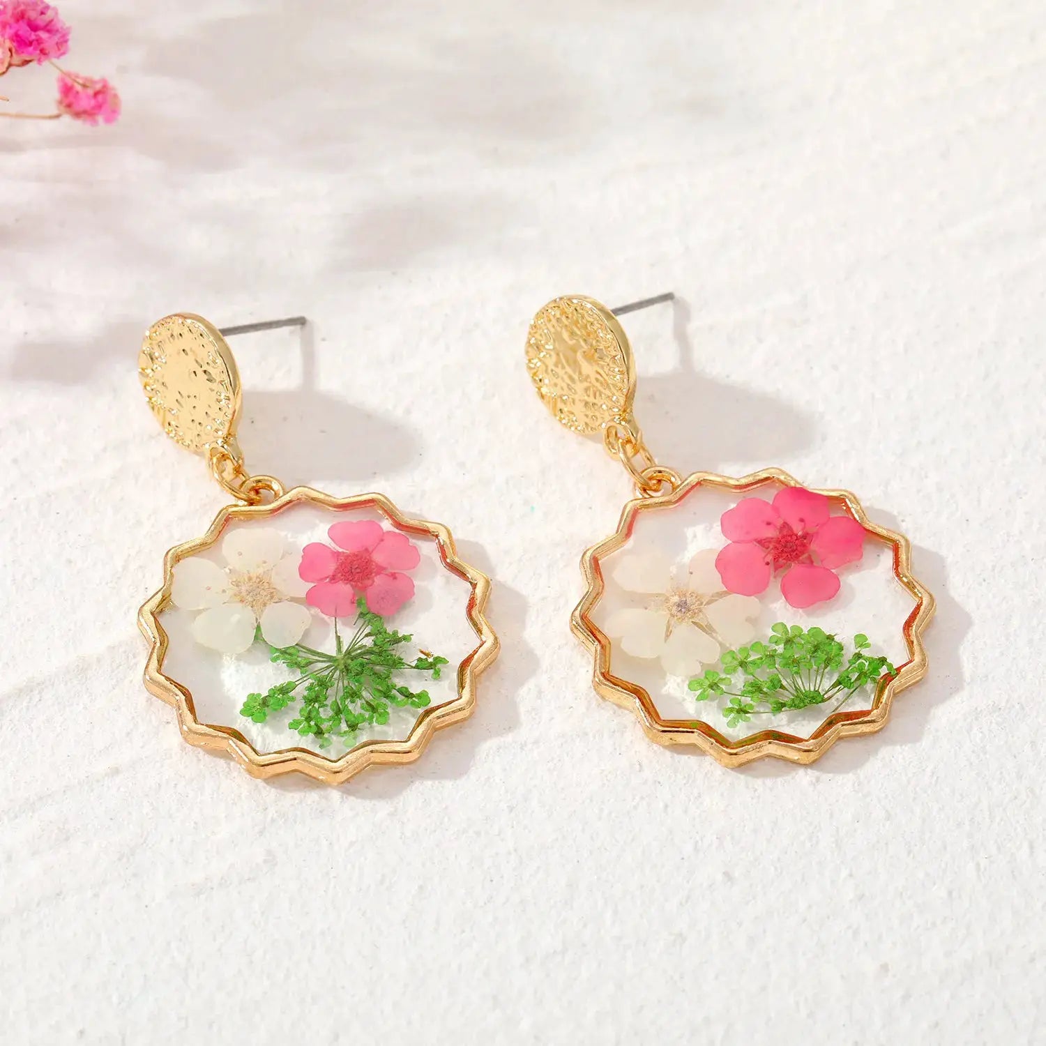 Pair of gold-tone dangle earrings with scalloped epoxy resin frames containing pink and white pressed flowers.