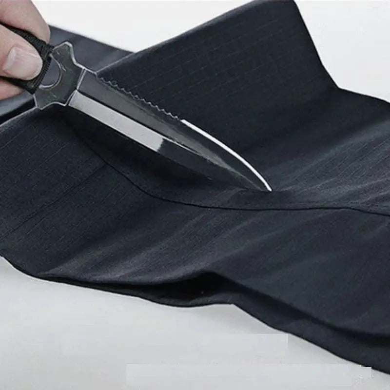 Men's black cargo pants fabric being cut with a knife