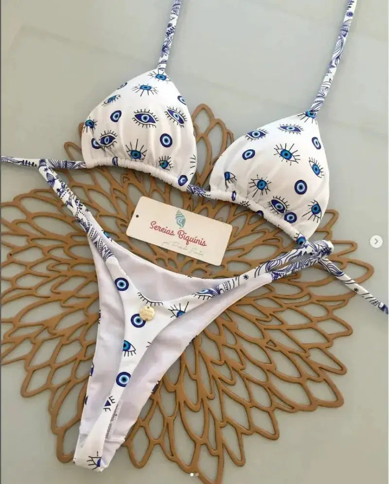 2-piece bikini set by Simples Market, white with blue eye pattern, halter triangle top and thong bottoms.