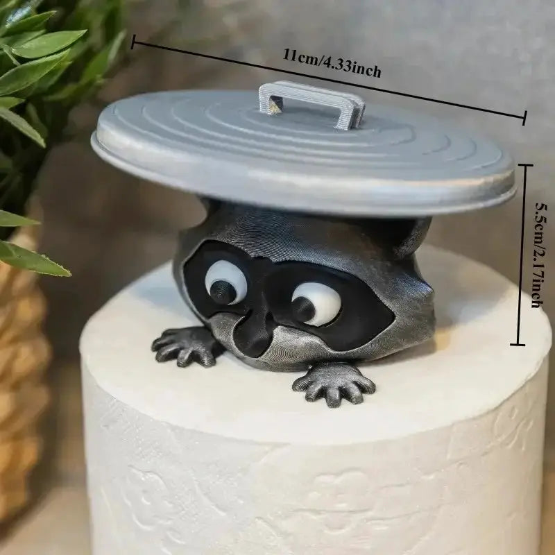 Toilet paper holder with gray raccoon figure peeking from under a round metal lid, Simples Market