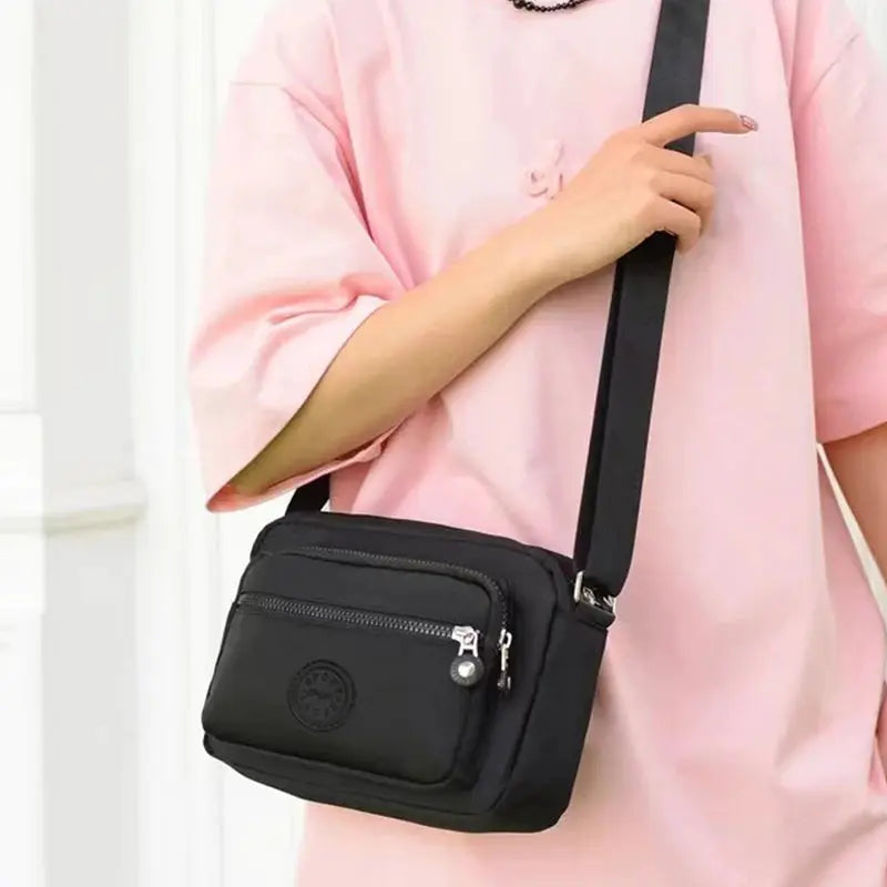 Crossbody bag by Simples Market, black with a front zip pocket and logo patch; adjustable strap.