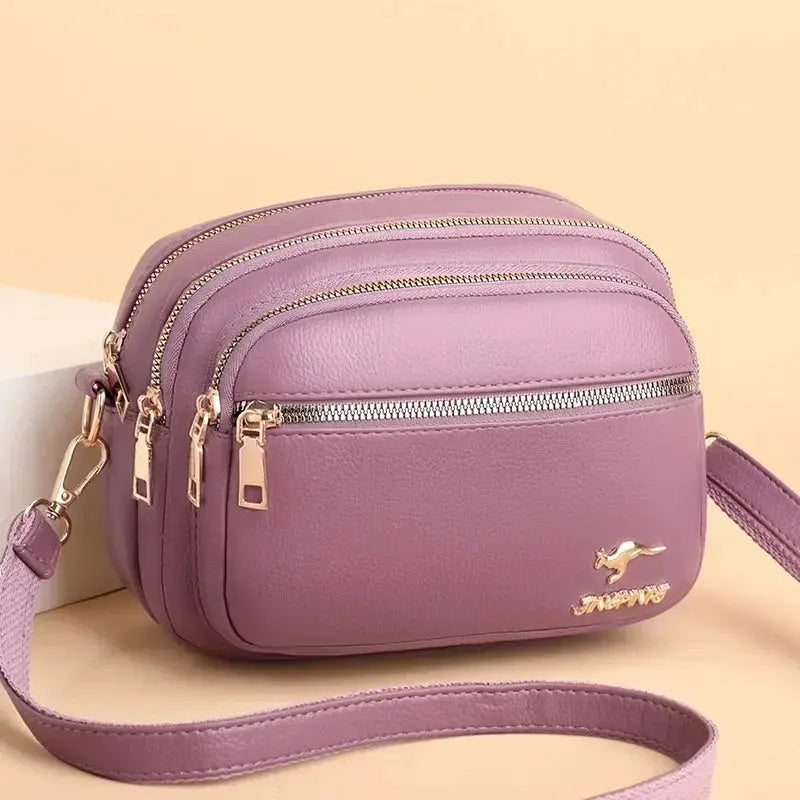 Crossbody bag by Simples Market in lavender leather with multiple zip pockets and gold hardware.