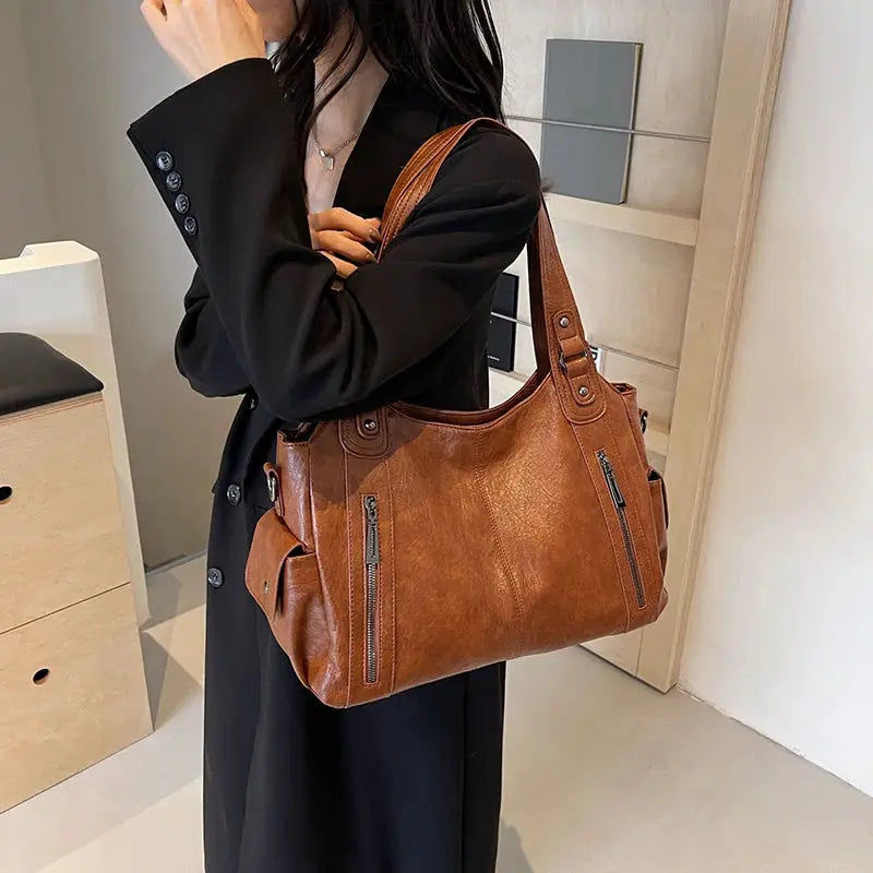 Soft interior compartment shoulder bag in brown PU leather with front zip pockets and top handles by Simples Market