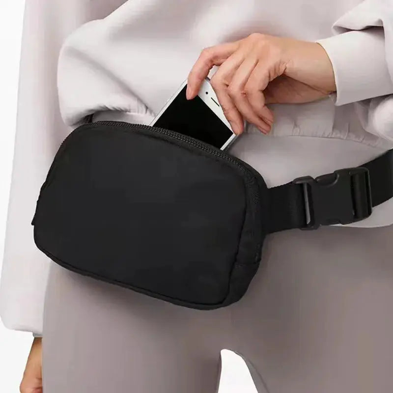 Black waist bag with zipper; adjustable belt strap worn at the hip, phone tucked inside.
