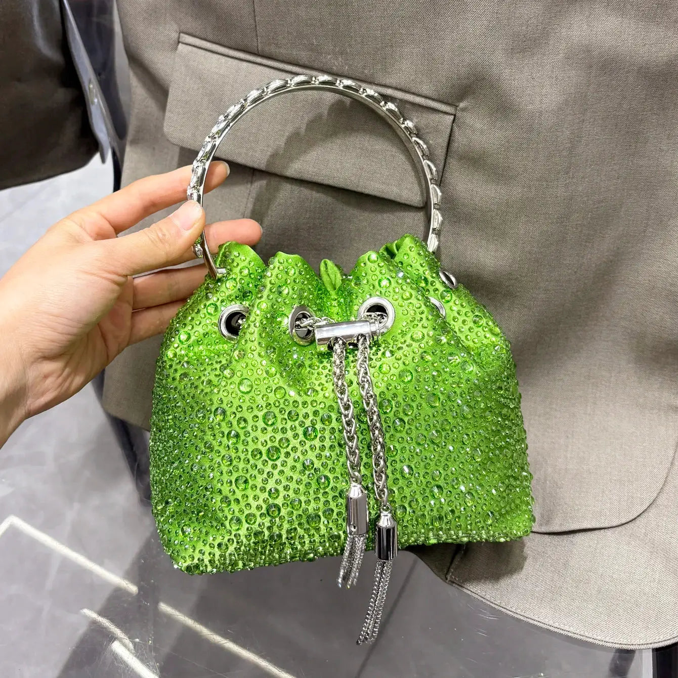 Green rhinestone bucket clutch with a silver ring handle and chain tassels.