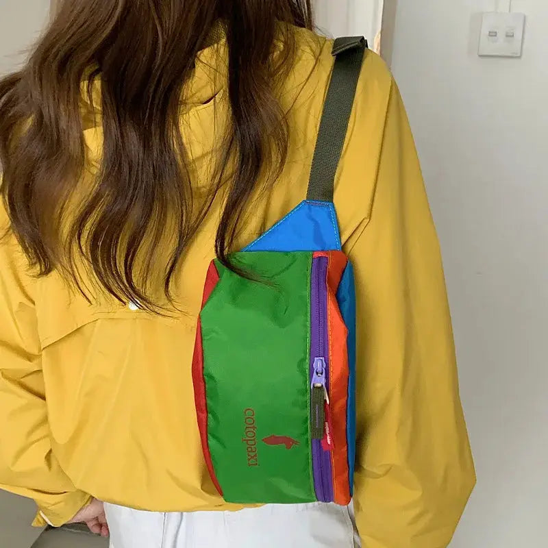 Cotopaxi waist bag in green with blue top panel and purple zipper, worn crossbody.