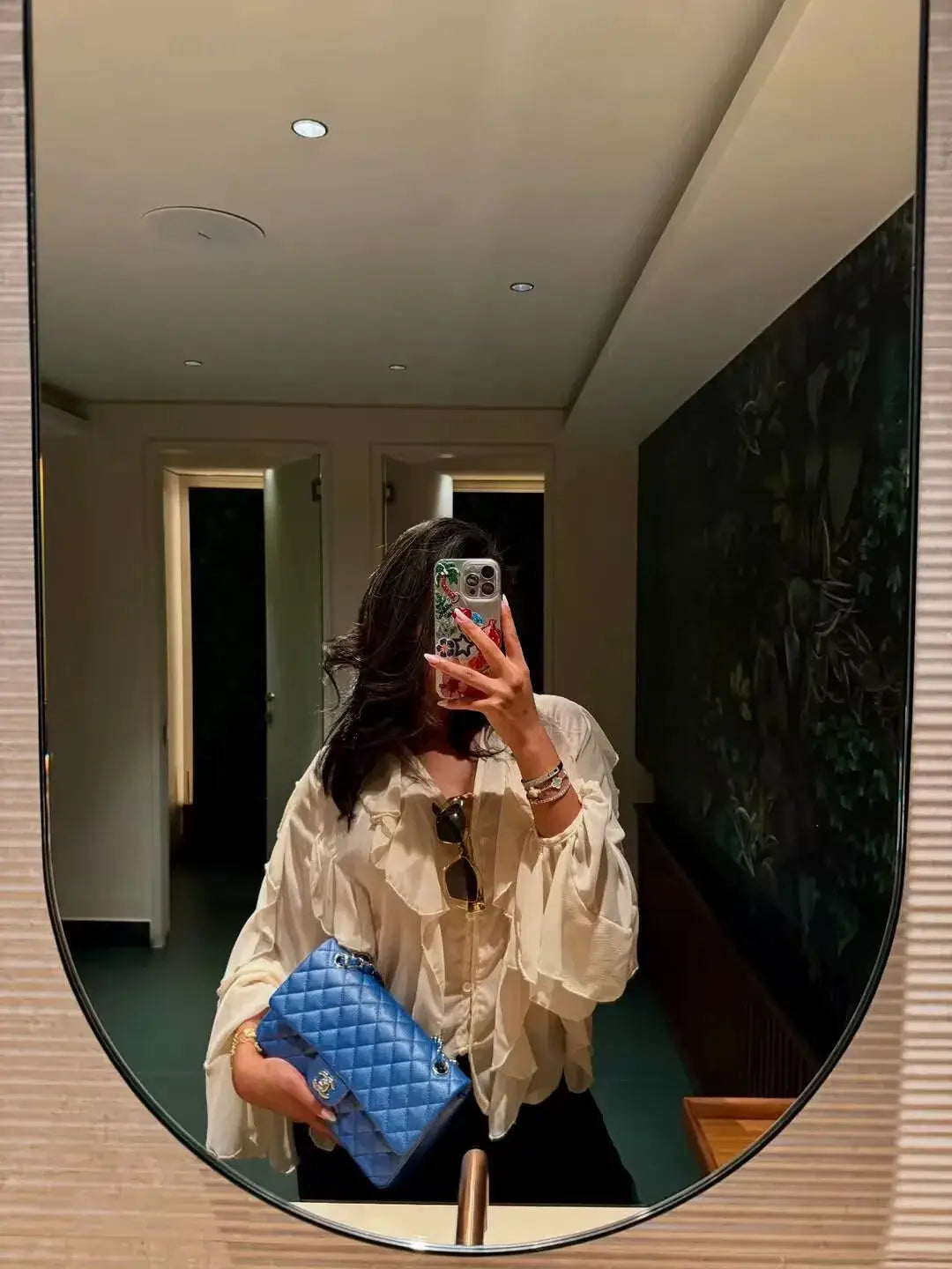 Women's white ruffle blouse with long sleeves and loose fit; paired with a blue quilted handbag