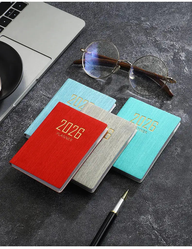 A7 pocket planners set of four 2026 planners in red gray teal and blue with a laptop and glasses nearby