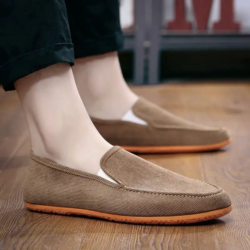 Two tan canvas loafers with orange soles, slip-on driving-style men's shoes.