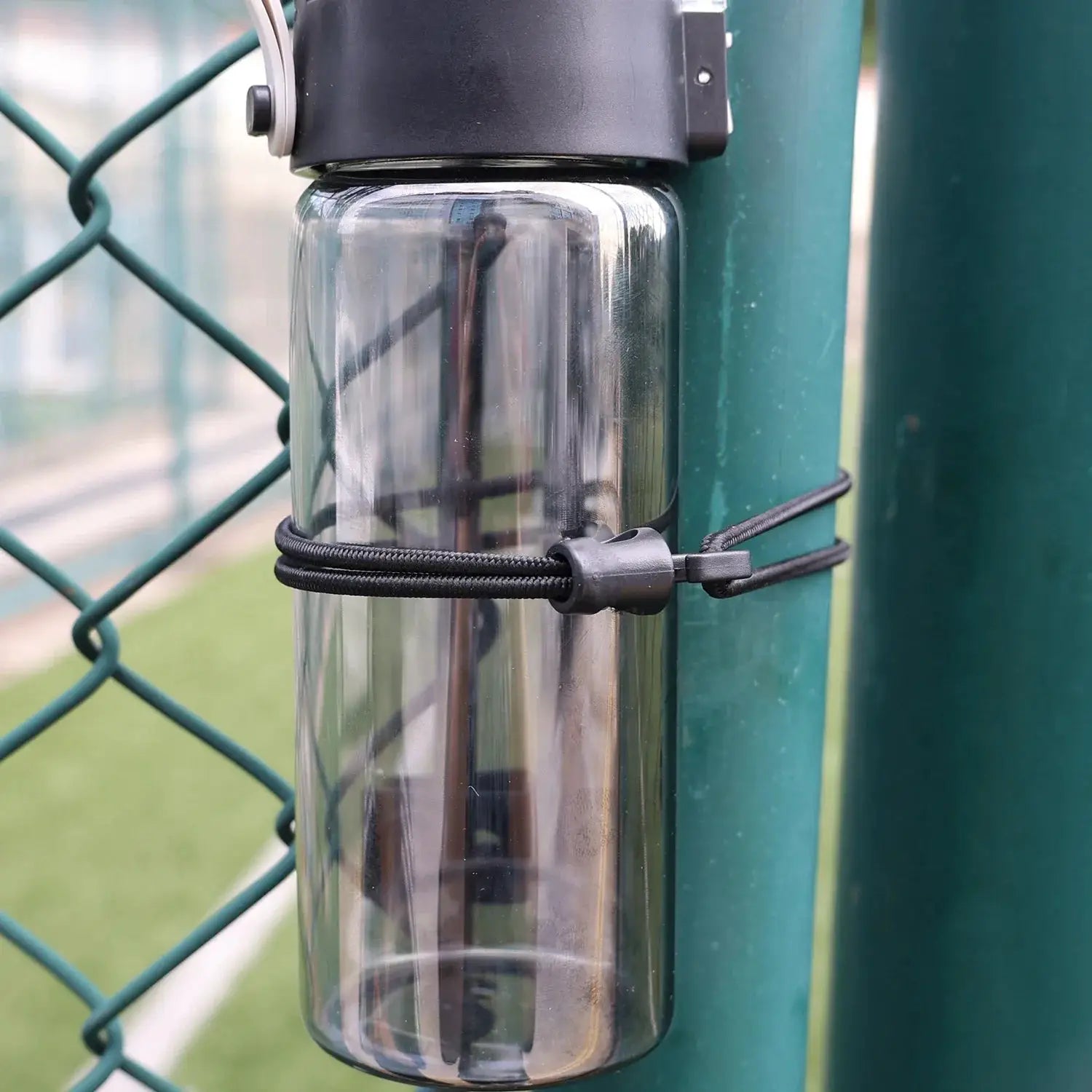 Bungee cord with hooks, black elastic, secured to a green fence post