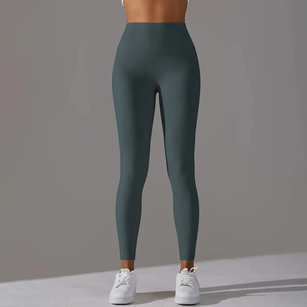 High-waist leggings in dark teal, full-length gym tights on a model with white sneakers