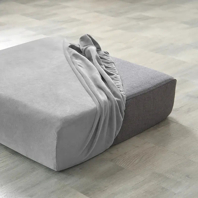 Plush light-gray sofa slipcover with elastic edges on a square ottoman, two-tone gray.