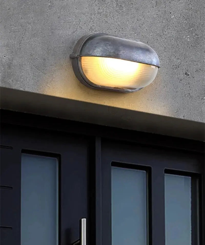 Outdoor retro LED wall lamp with weathered metal finish and ribbed glass shade, wall-mounted above a doorway.