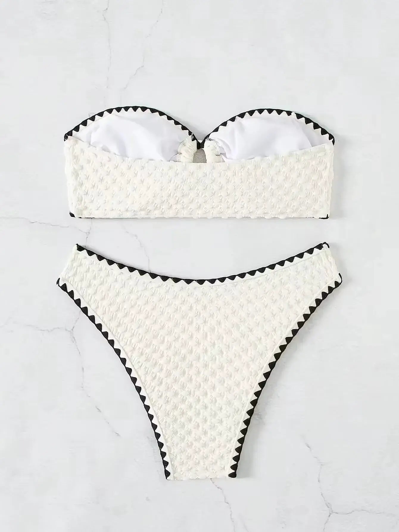 White two-piece strapless bandeau bikini set with textured fabric and black triangular trim on top and bottom.
