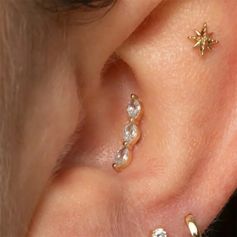 Three gold-tone earrings: star stud, curved CZ climber with three marquise stones, and small CZ hoop