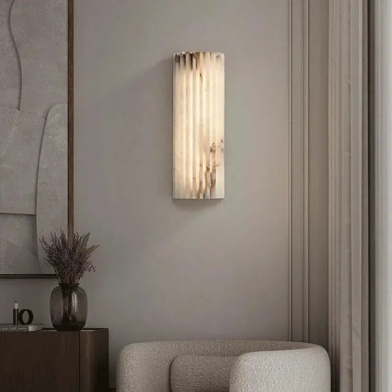 Modern minimalist marble wall lamp; vertical ribbed cream marble with brown veining, warm glow on gray bedroom wall.