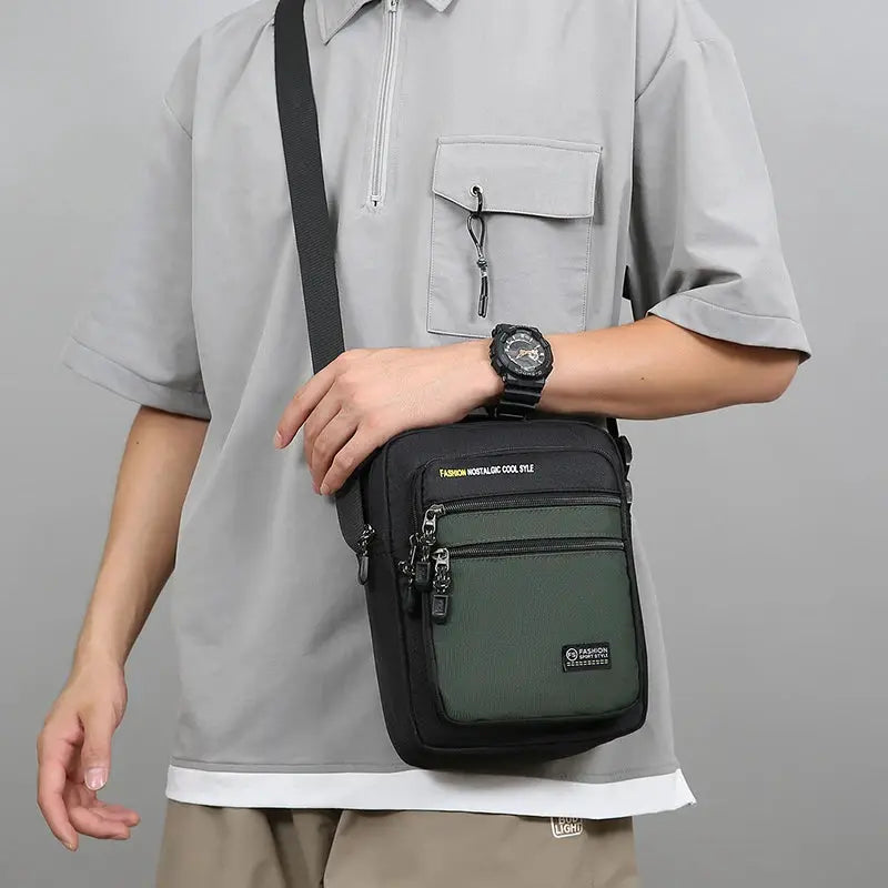 Men's Oxford crossbody bag, black body with green front panel, multi-pocket storage, worn crossbody.