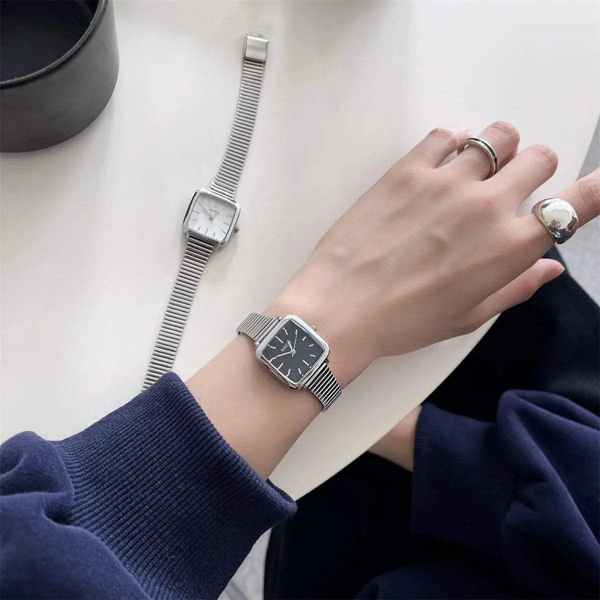 Simples Market stainless steel women's quartz watches set; black-dial wristwatch on wrist, white-dial watch on table (2).