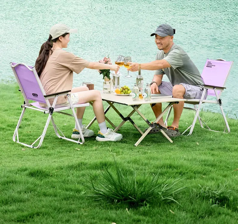 Pair of BISINNA outdoor folding camping chairs in purple with white metal frames beside a portable picnic table.