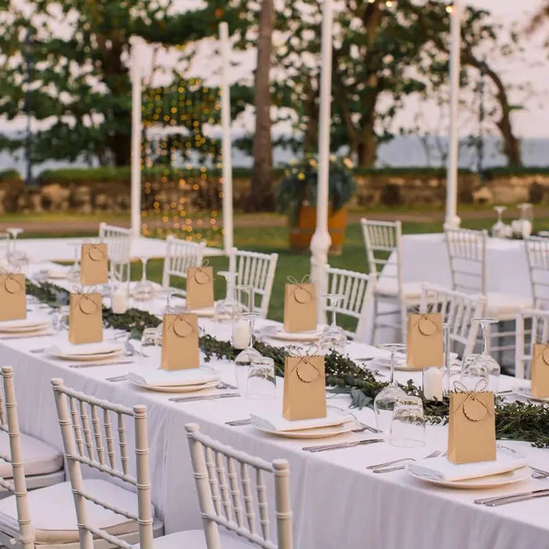 Kraft paper gift bags with rope handles lined along an outdoor wedding reception table, ready as party favors