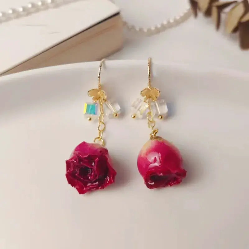 Pair of red rose drop earrings with epoxy resin blooms, gold hooks, and crystal bead accents