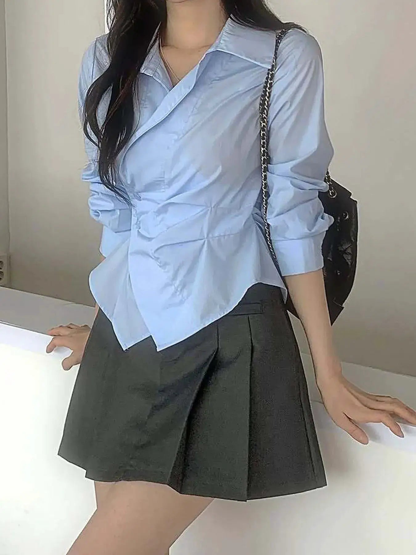 Simples Market designer irregular long-sleeve light-blue polo blouse with wrap front, paired with a black skirt.