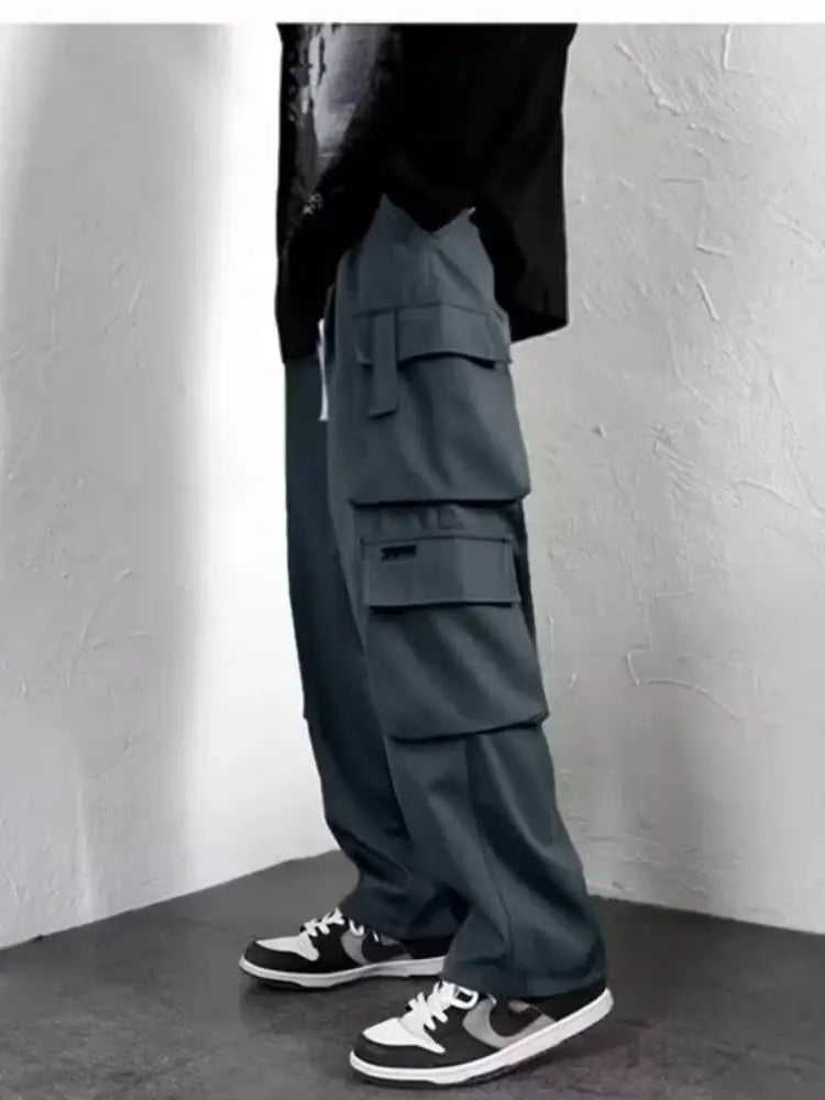 Men's blue-gray cargo jogger pants with multiple pockets and a baggy fit, shown with sneakers.
