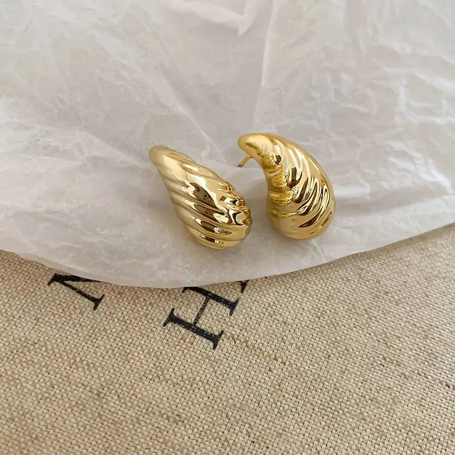 Gold-toned irregular pleated oval acrylic stud earrings, unisex pair.
