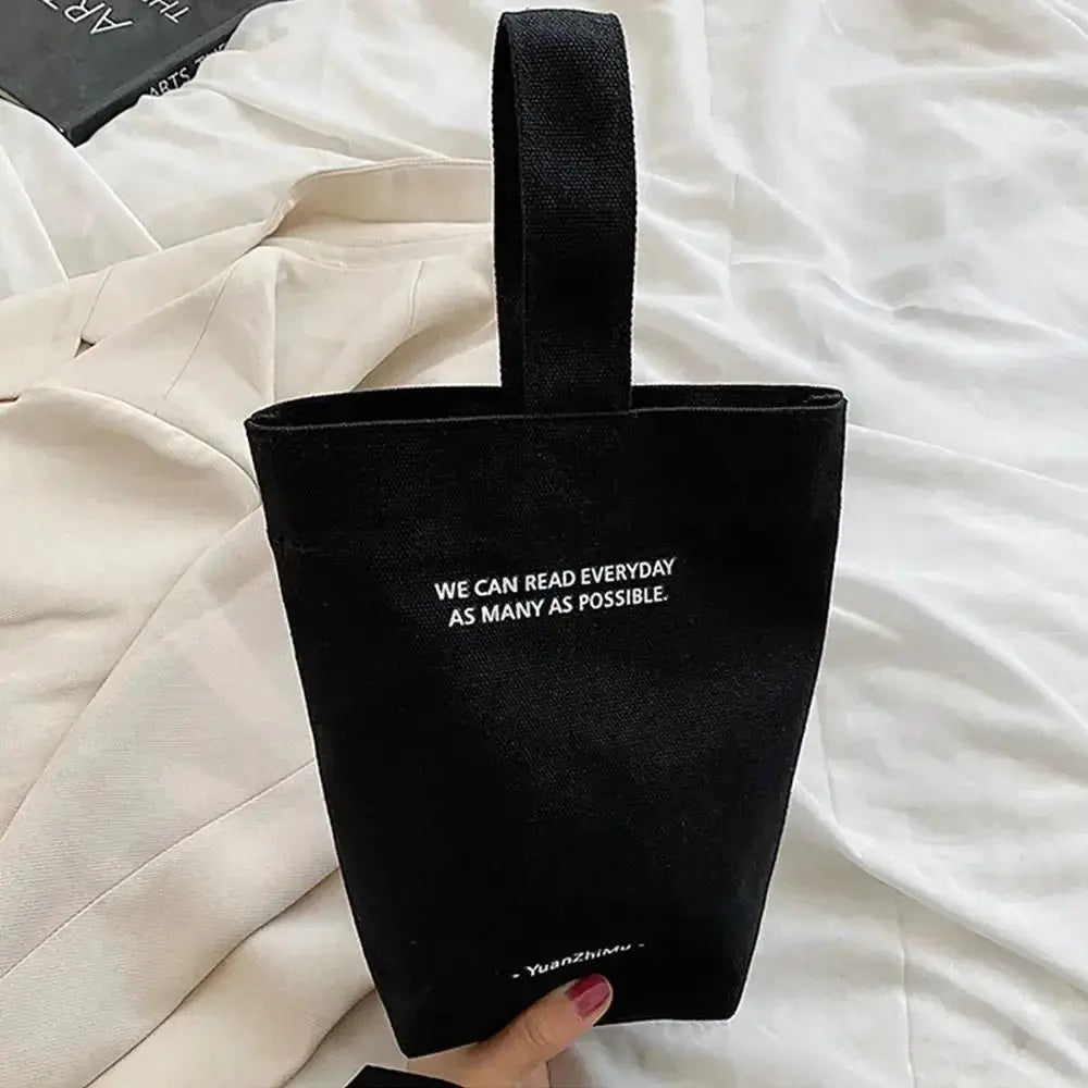 Casual canvas handbag by Simples Market with top handle and white slogan text, large-capacity tote.
