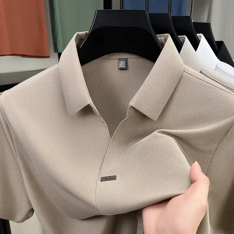 Men's polo shirts on hangers; four solid-color short-sleeve polos with ribbed fabric in neutral tones.