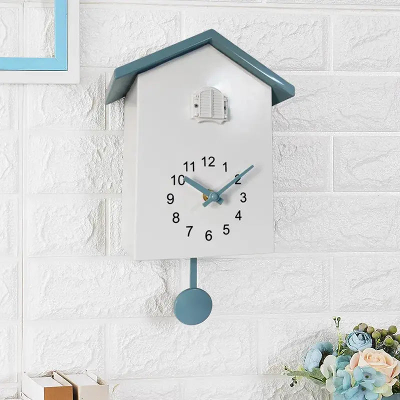 Cuckoo quartz wall clock, birdhouse style with white body, blue roof and blue hands, pendulum on white brick wall