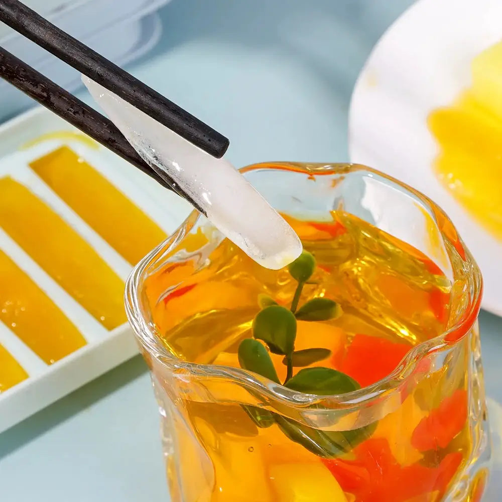 Long bar ice cubes mold; clear cylindrical ice cube held by chopsticks over an orange beverage in a glass.