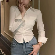 White women's button-down shirt with collar and long sleeves, paired with jeans.