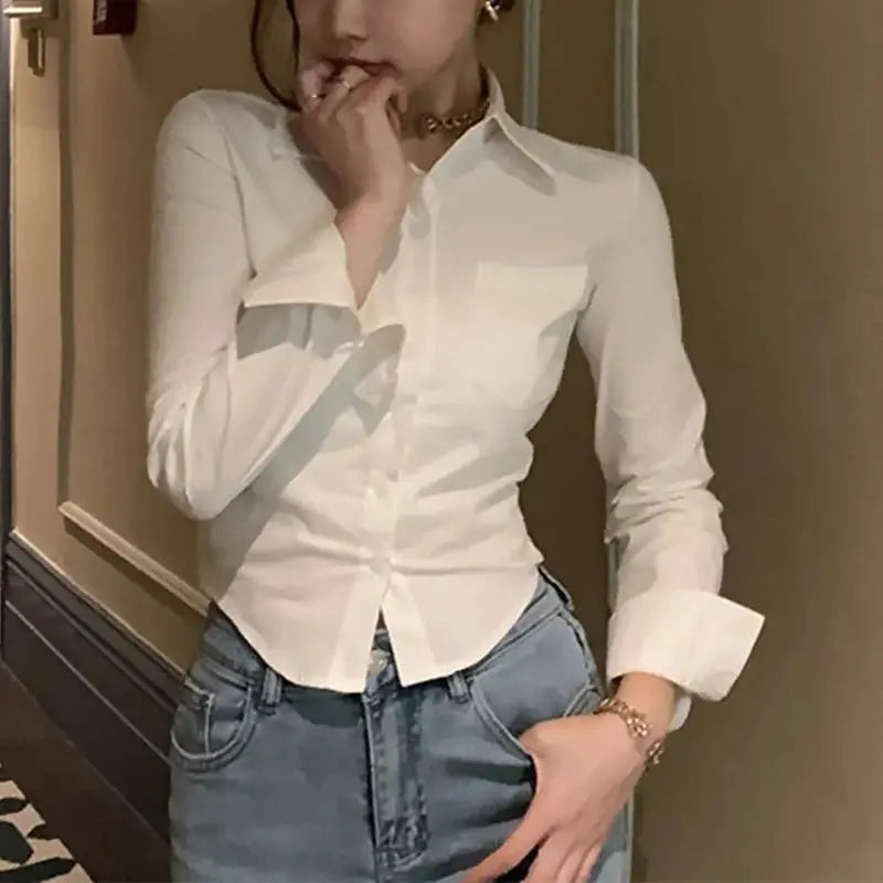White women's button-down shirt with collar and long sleeves, paired with jeans.