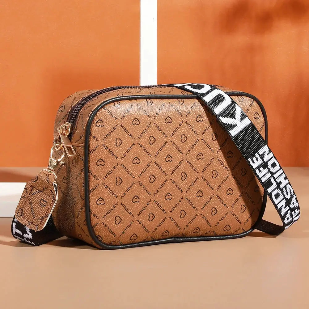Crossbody bag by Simples Market; tan faux leather with black trim and a bold black-and-white branded strap