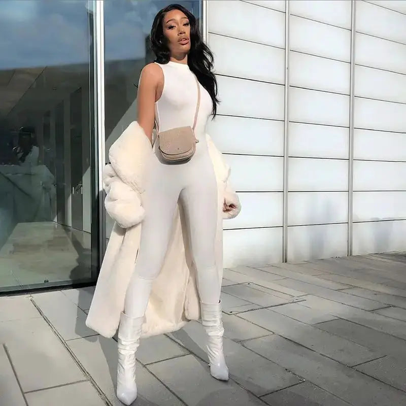 Pencil jumpsuit in white with white fur coat, beige crossbody bag, and white knee-high boots